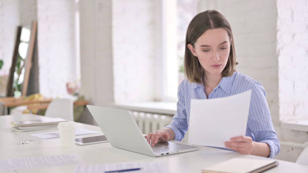 istock Focused Young Woman Reading Documents and Working on Laptop 1219498615