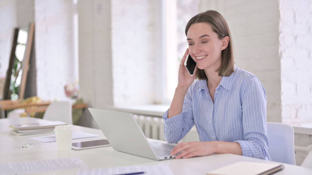 istock Beautiful Young Woman Talking on Smartphone in Modern Office 1219498648