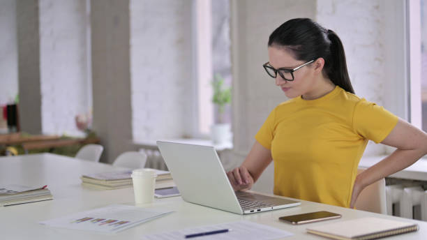 Tired Young Female Designer having Back Pain in Modern Office