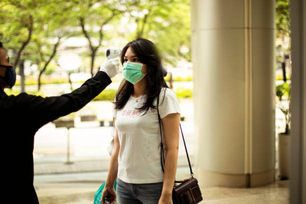 Asian woman checked with thermometer to control the temperature required to be checked in quarantine security guard measuring temperature of young woman  with infrared thermometer before entering a office, in Jakarta. covid thermometer stock pictures, royalty-free photos & images