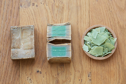 Flat lay overhead shot of an Aleppo bar soap and cuts showing its green color on a wooden background. Concept of hygiene and dermatology, covid-19 and virus prevention, sustainable and zero waste life