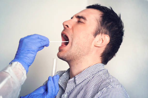 test adn. docteur faisant coronavirus covid 19 test pour le patient masculin. prélever un échantillon de salive d’un homme. collecte de mucus de la gorge pour la recherche en laboratoire. - human saliva photos et images de collection