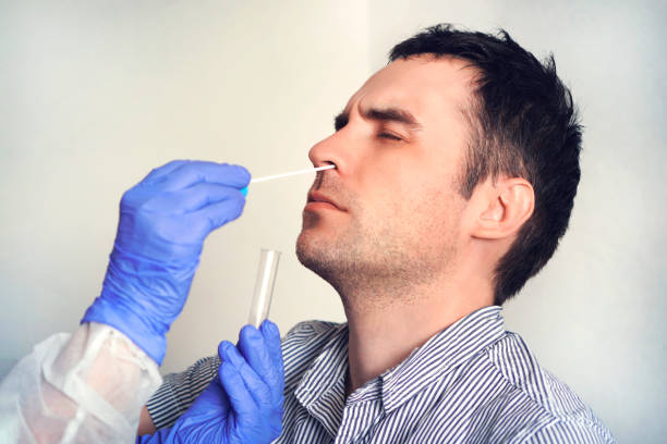 コロナウイルス感染の可能性を検査するために人から鼻綿棒を取る防護服の医師。ウイルス感染のための鼻粘液検査。 - nasopharynx ストックフォトと画像
