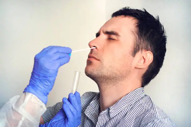 Photo of doctor in a protective suit taking a nasal swab from a person to test for possible coronavirus infection. Nasal mucus testing for viral infections.