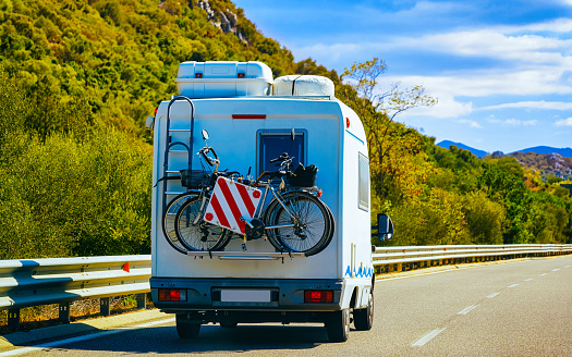 Vacation trip with Caravan Car with bicycle on road, Italy. Camper and Summer drive on highway. Holiday journey in rv motorhome for recreation. Motor home minivan motion ride on nature. Scenery.