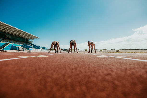 Athletes at starting line on running track Three young athletes at starting position ready to start a race. Sports women ready for race on racetrack. relay stock pictures, royalty-free photos & images