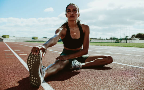 Female runner doing stretching exercises sitting on the track