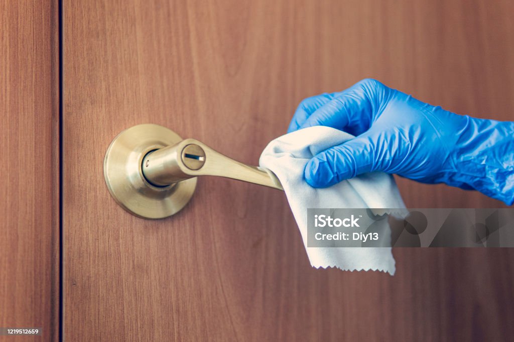 A woman's hand wipes the door handle with wet rag. The maid is washing the doorknob. Prevention of coronavirus and bacterial infections A woman's hand wipes the door handle with a wet rag. The maid is washing the doorknob. Prevention of coronavirus and bacterial infections Water Surface Stock Photo