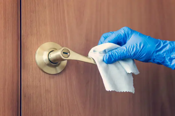 A woman's hand wipes the door handle with a wet rag. The maid is washing the doorknob. Prevention of coronavirus and bacterial infections