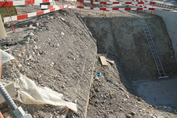 istock Construction pit or shaft on a civil engineering construction site with a metal ladder for better access surrounded by barrier planks in red and white. 1219512851