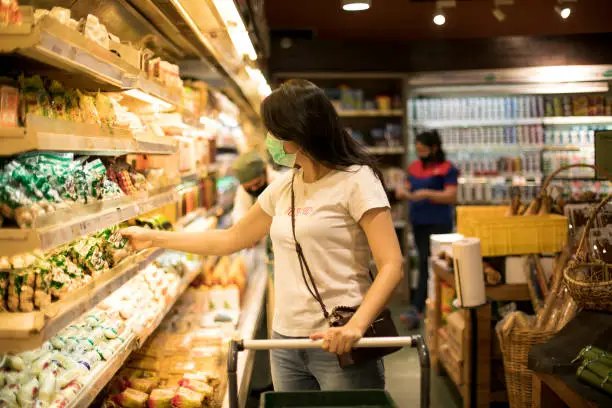 Photo of Young woman shopping in a grocery store and wearing protective medical mask