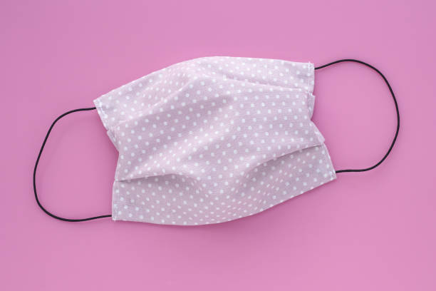Protective reusable face mask from textile on pink background. Handmade polka dot mask from infection. stock photo