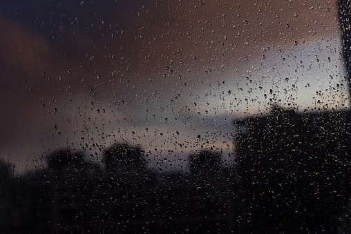 Slowly dripping raindrops and blurred lights from the windowpane