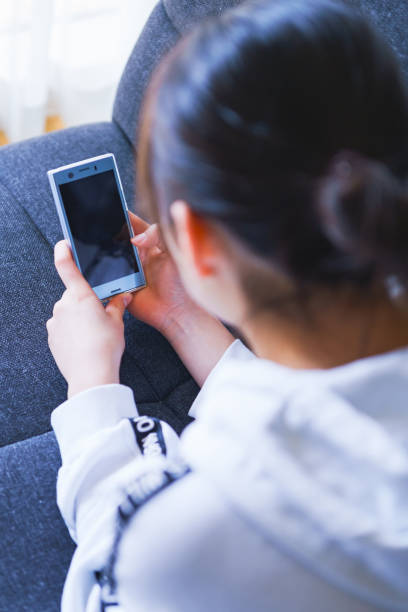 ragazza giapponese che guarda lo smartphone sul divano di casa - smart phone china mobile phone asia foto e immagini stock