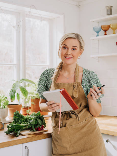 istock Woman at home in kitchen with vegetables and notebook cookbook 1219522977