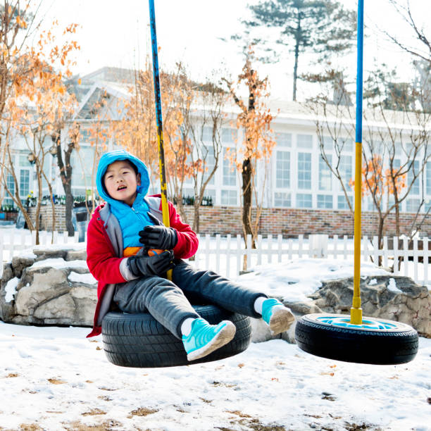 Boy playing on tire swing in winter day.
