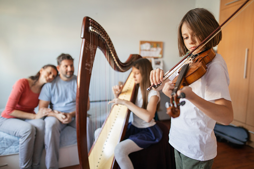 Boy and girl playing harp and violin at home for they parent. They performing music in children room for fun and joy.
Photo taken during quarantine because of corona virus outbreak.