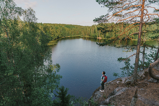 Young Caucasian woman sitting, looking at lake in Finland and drinking tea