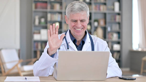 istock Cheerful Senior Doctor Doing Video Chat on Laptop while Sitting in Office 1219527248