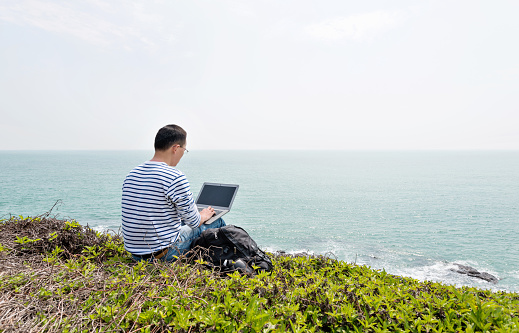 Man using laptop by the sea.