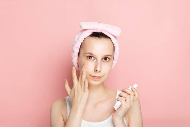 istock Young girl without makeup apply face moisturizer lotion on pink background 1219530200