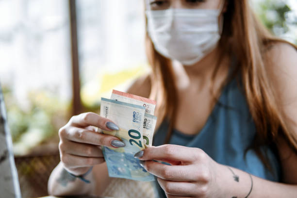low angle view of masked young woman counting group of euro banknotes - market european culture caucasian stock market imagens e fotografias de stock