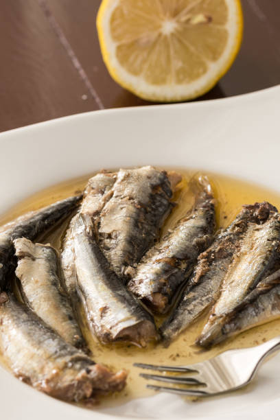 istock Marinated sardines in oil served on a white plate with metal fork and lemon 1219535181