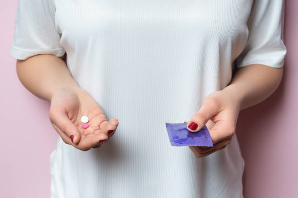 contraceptive means: a condom and birth control pills in a hand on a pink - sex education condom contraceptive sex imagens e fotografias de stock