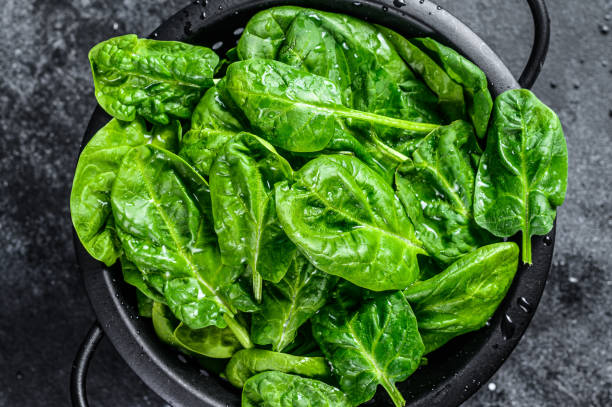 istock Young raw spinach in a colander. Black background. Top view 1219550061