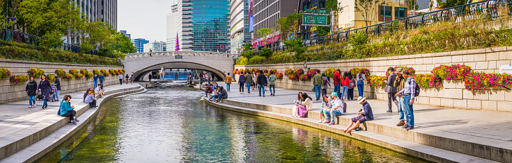 Locals and tourists enjoying the sunshine on the banks of the Cheonggyecheon Stream between the soaring skyscrapers of downtown in the heart of Seoul, South Korea’s vibrant capital city.