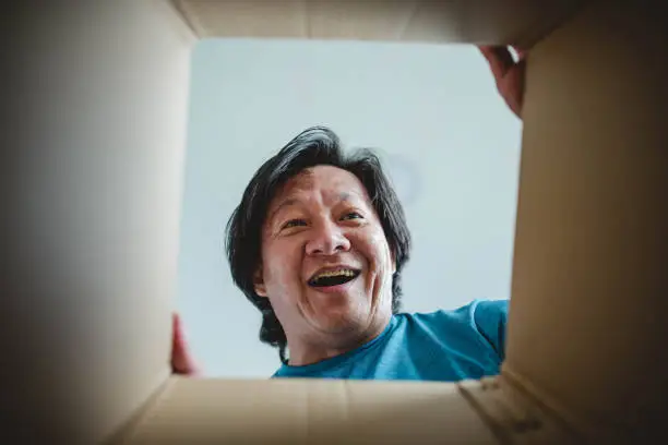 Photo of Asian man surprised is looking inside cardboard box