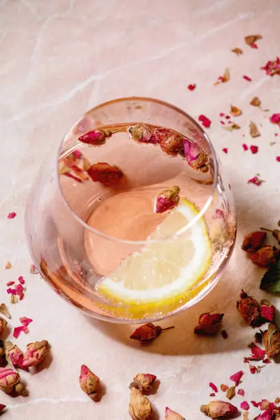Cocktail glasses of pink rose champagne, cider or lemonade with dry rose buds and lemon. Pink marble background. Close up