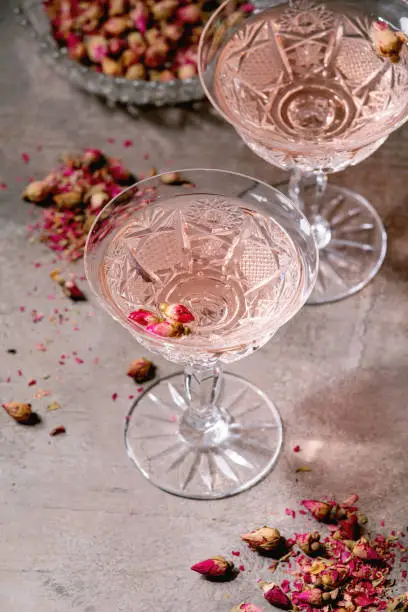 Crystal vintage glasses of pink rose champagne, cider or lemonade with dry rose buds. Grey texture background.