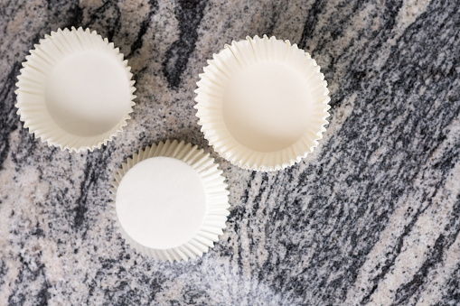 Flat lay above empty white cup cake cases containers on the grey granite marble background.