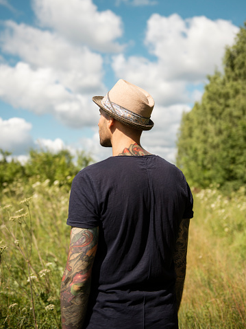 Back view of young man standing in field looking at scenic view during sunny summer day