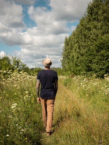 Back view of young man walking in field during sunny summer day