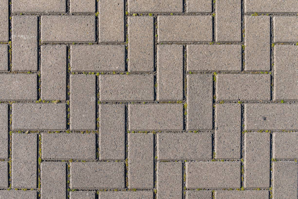 Concrete paving stones in grey during warm sunlight laid out in regular pattern texture