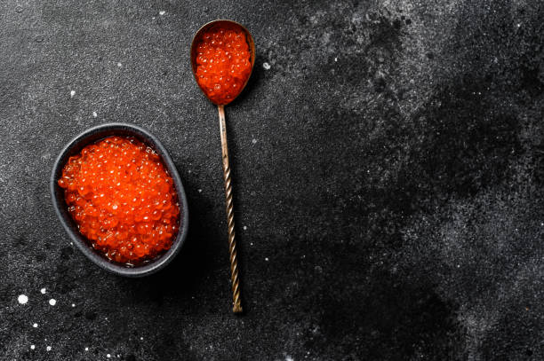 istock Salmon red caviar in an exquisite spoon. Black background. Top view. Copy space 1219560122