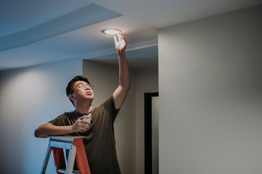 an asian chinese mid adult male changing light bulb in living room, apartment home