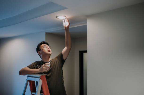 uma lâmpada asiática chinesa média adulto trocando lâmpada na sala de estar, casa apartamento - led lighting equipment light bulb installing - fotografias e filmes do acervo