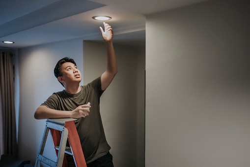 an asian chinese mid adult male changing light bulb in living room, apartment home