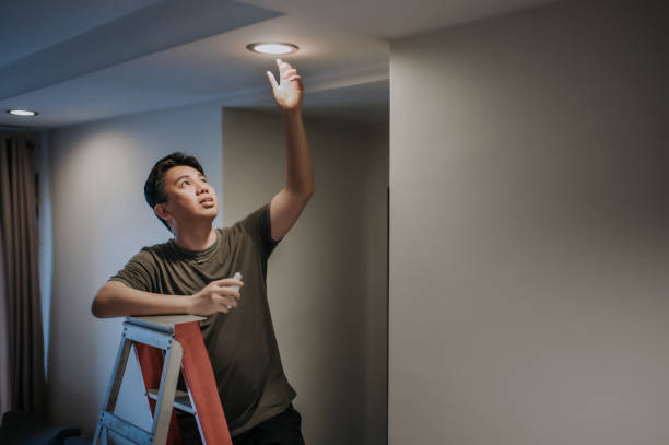 uma lâmpada asiática chinesa média adulto trocando lâmpada na sala de estar, casa apartamento - led lighting equipment light bulb installing - fotografias e filmes do acervo
