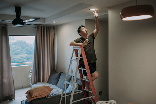 an asian chinese mid adult male changing light bulb in living room, apartment home