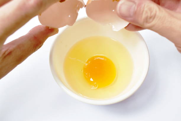 istock hand opened shell and raw egg with yolk in cup on white background 1219563917