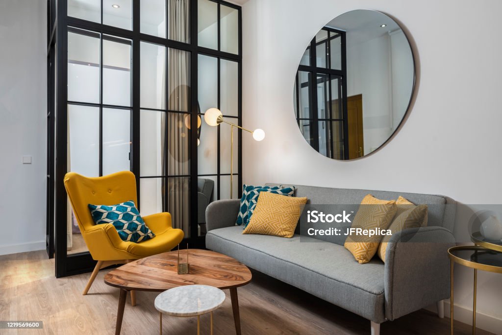 Colorful and cozy living room with a designer armchair and sofa along with a round decorative mirror and glass wall. Mirror - Object Stock Photo
