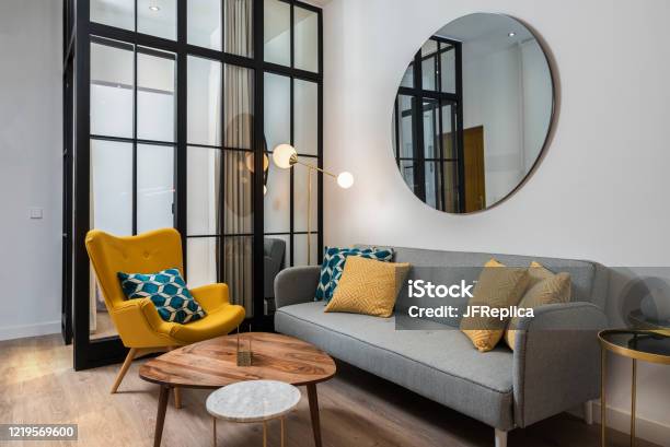 Colorful And Cozy Living Room With A Designer Armchair And Sofa Along With A Round Decorative Mirror And Glass Wall Stock Photo - Download Image Now