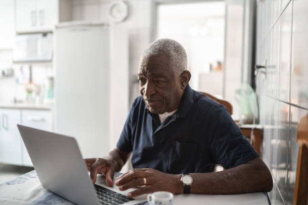 старший человек, работающий за ноутбуком - people casual emotional stress table стоковые фото и изображения