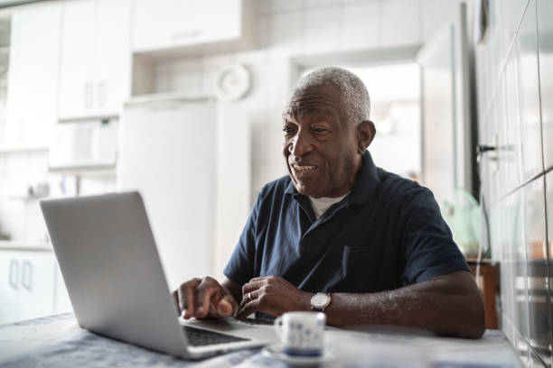 hombre mayor trabajando en la computadora portátil en casa - viejo fotografías e imágenes de stock