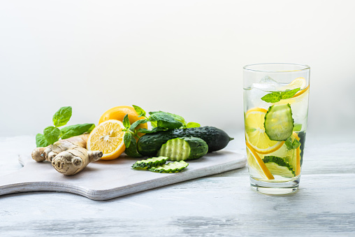 Detox Sassy water with lemon, cucumber, mint. A glass of clean, cool and fresh drink stands on a white wooden table with ingredients on board. Strengthening immunity, diet. Still life with copy space.
