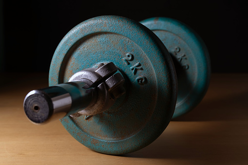 Old vintage variable weight dumbbell over wood against black background